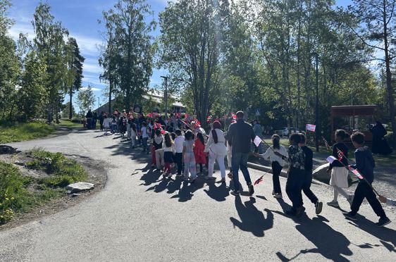 en gruppe mennesker som går på en vei med trær på hver side