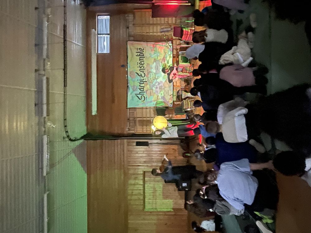 en gruppe mennesker som sitter i et rom med en person som står på en scene med en mikrofon og